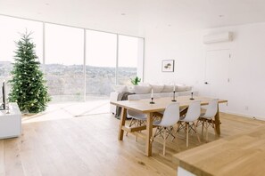 A modern interior with a dining area, white furniture, a Christmas tree, and a large window offering a view.