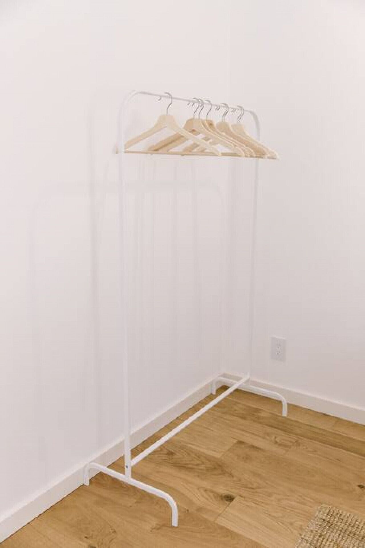 Un armario metálico blanco con perchas de madera, situado frente a una pared blanca con suelo de madera.