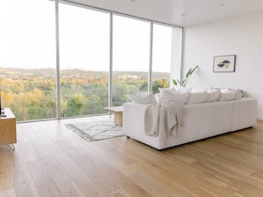 A modern living room with a large window, a white sofa, a wooden coffee table, and a plant.