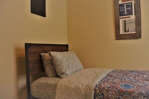 Un lit avec une literie à motifs et une tête de lit, un mur orné d’un tableau encadré et un mur à texture.