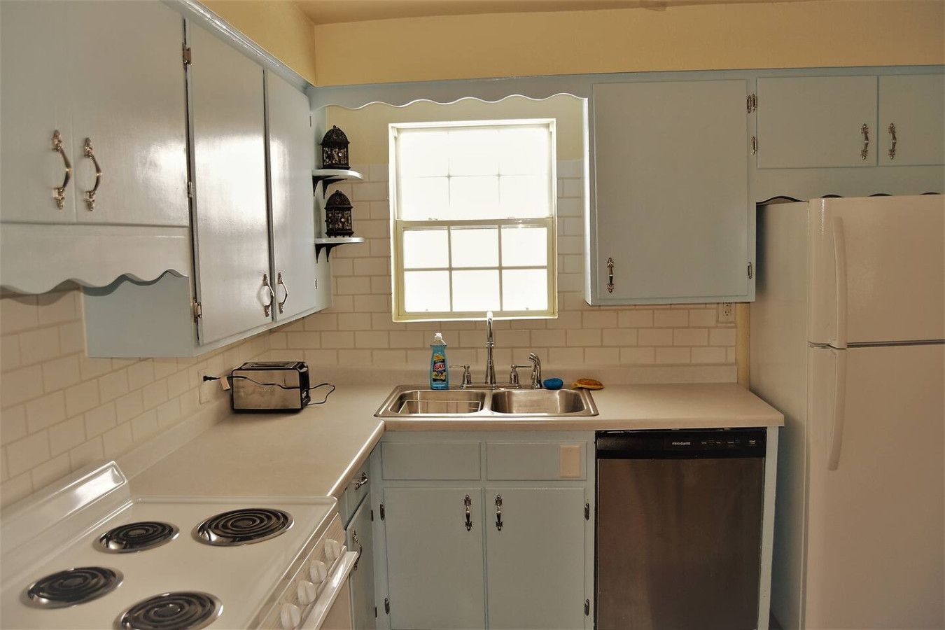 Una cocina compacta con electrodomésticos blancos, una ventana sobre el lavabo y armarios azul claro.