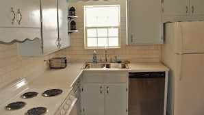 A compact kitchen with white appliances, a window above the sink, and light blue cabinets. - The Gateway: experience a stylish and welcoming lodging, perfect for groups. (Grand Forks)