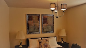 A hotel room with a bed, two nightstands, a chandelier, and two framed pictures on the wall. - The Gateway: experience a stylish and welcoming lodging, perfect for groups. (Grand Forks)