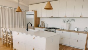 A modern kitchen with white cabinetry, a central island, a stove, and pendant lighting. - A modern light-filled home with views of the woods (Bonita)