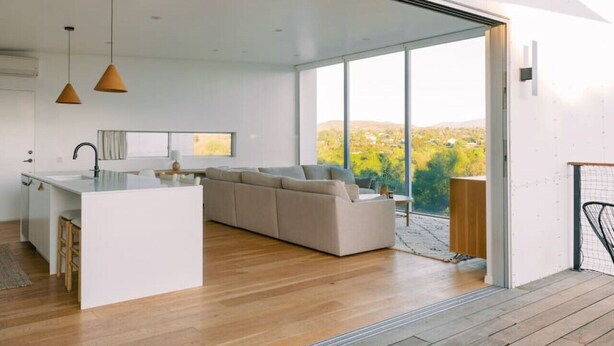 A modern interior with a kitchen, a sofa, and a view of a landscape. - A modern light-filled home with views of the woods (Bonita)