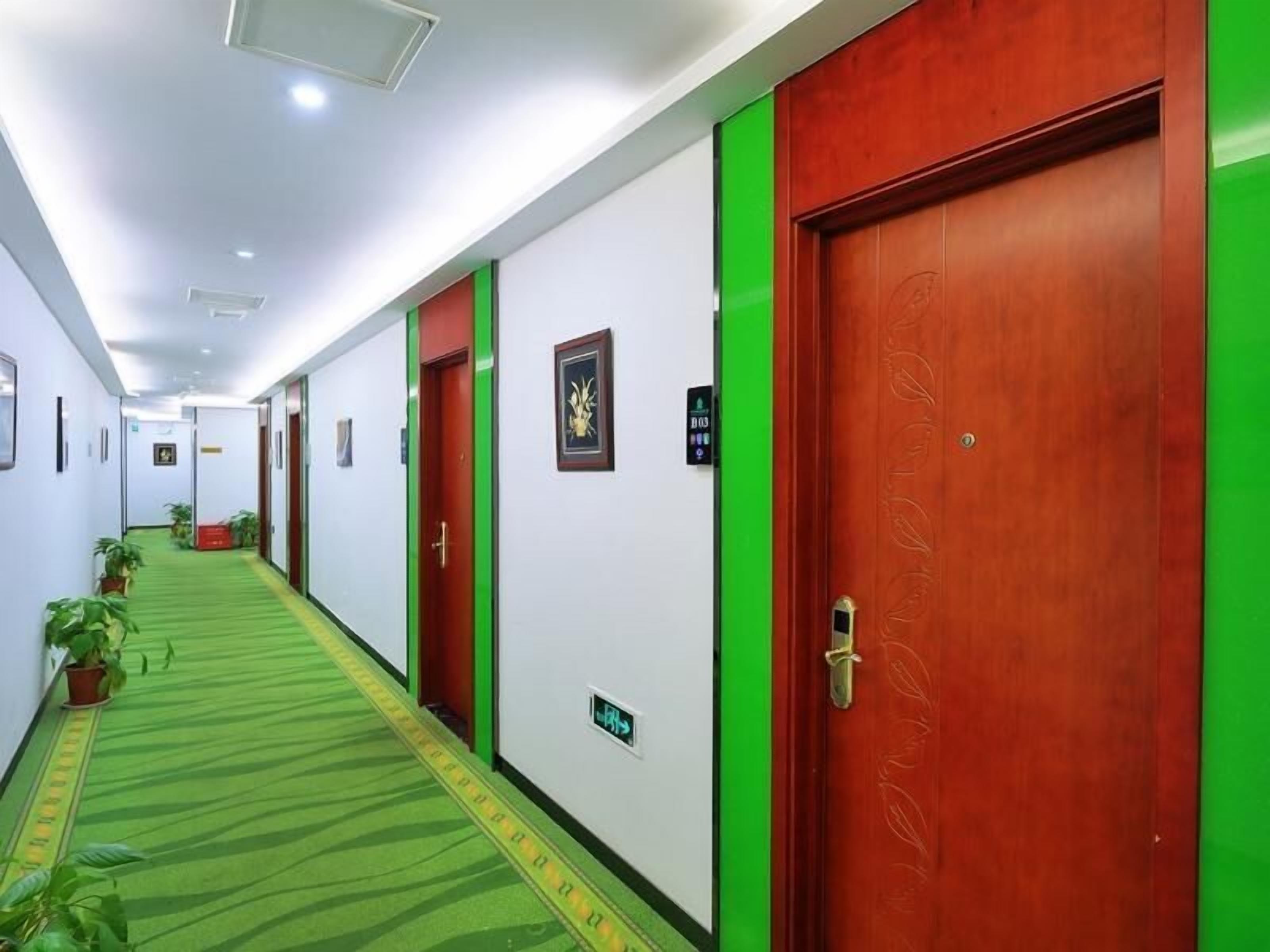 A hotel corridor with green carpet, red doors, and white walls.