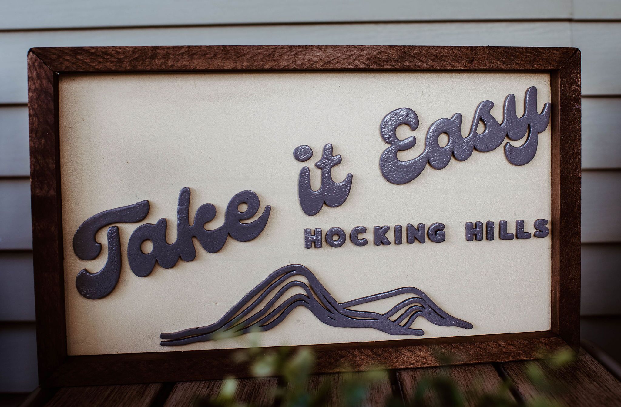 A framed sign with the text 'Take it Easy' and 'Hocking Hills' along with a mountain silhouette.