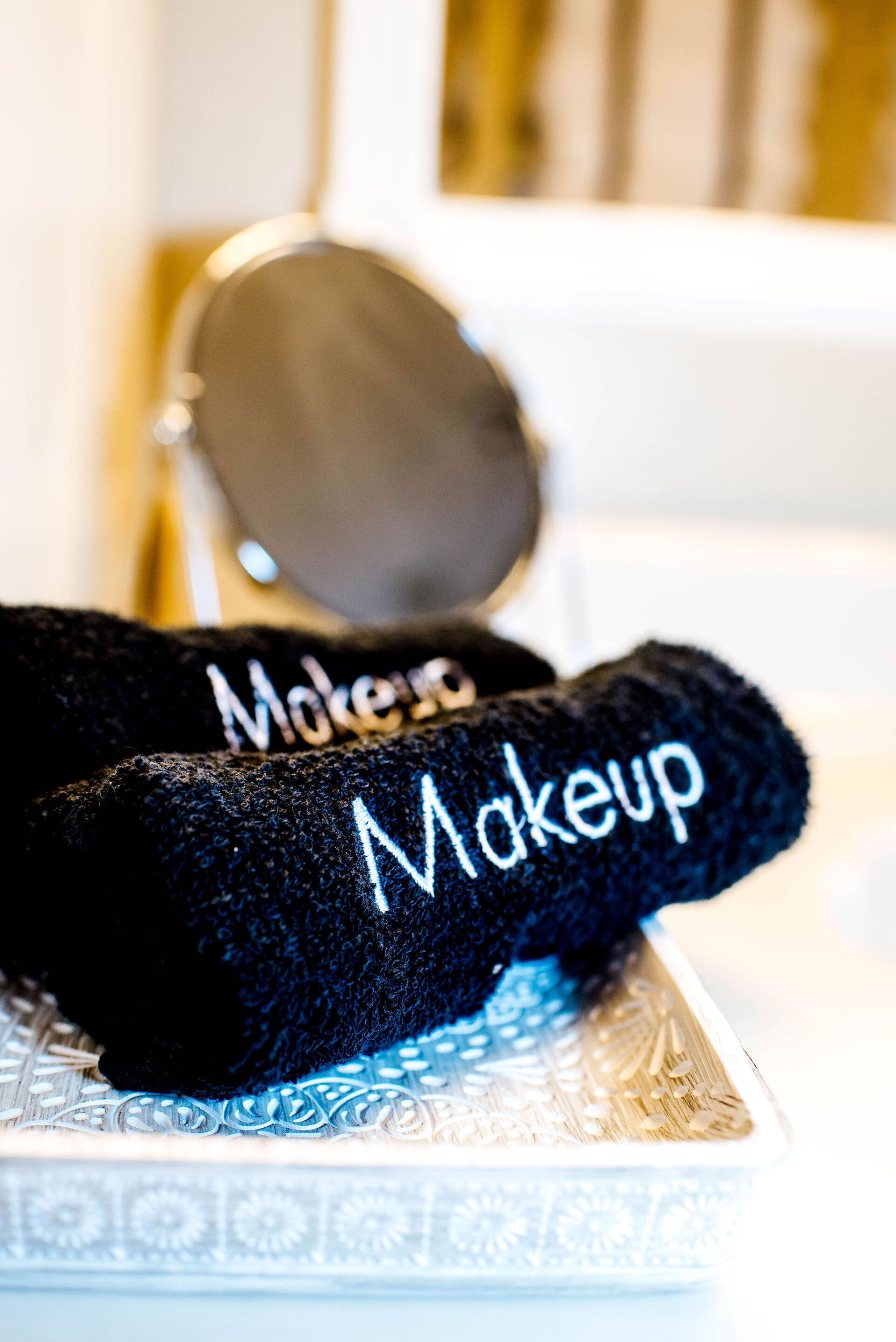 A pair of black makeup towels with the word 'Makeup' written on them, placed on a patterned tray.