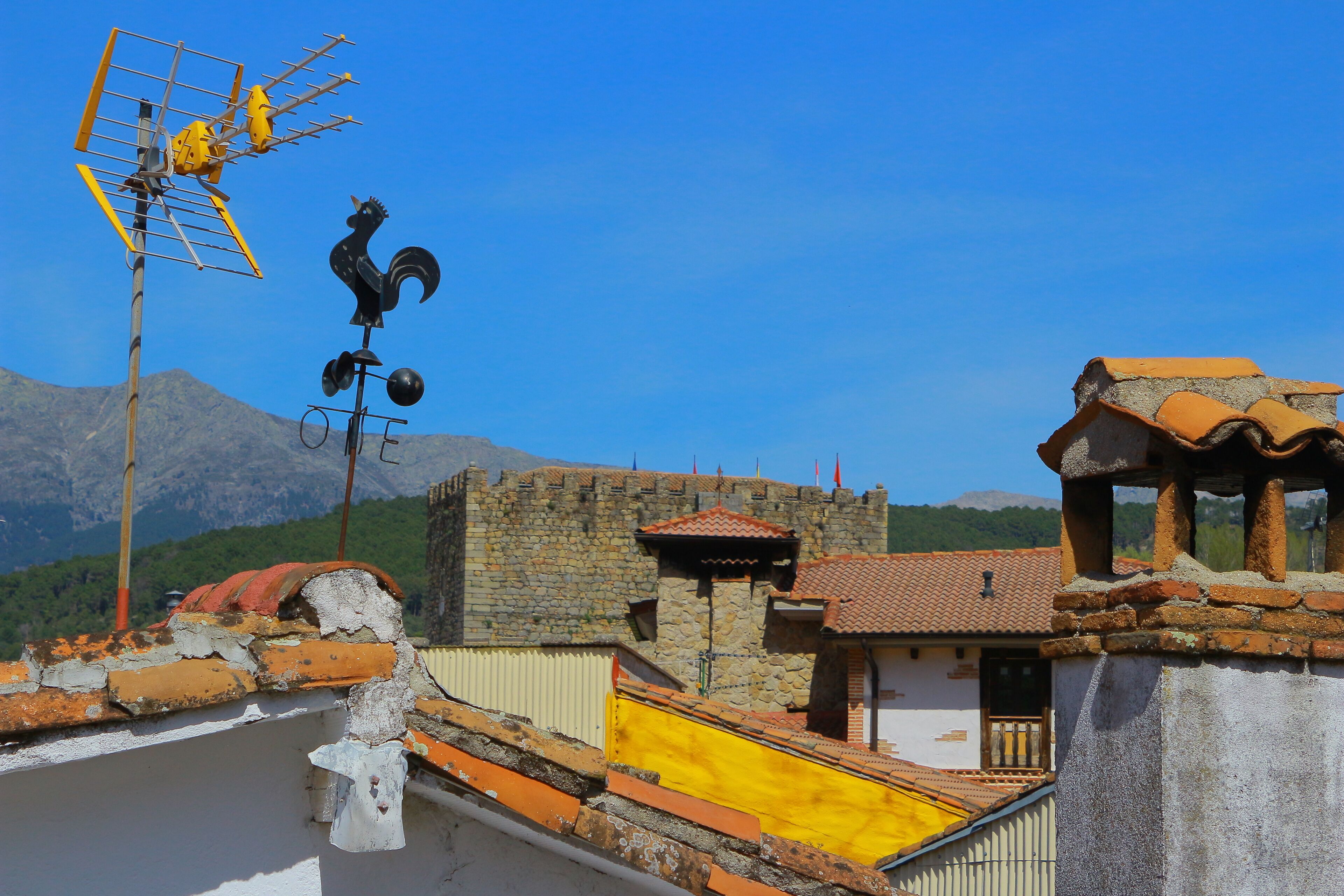 A traditional building with a stone wall and a yellow roof, a rooster sculpture, and a weather vane.