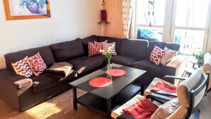Una sala de estar moderna con un sofá marrón oscuro, una mesa de centro y una silla. Hay un cuadro en la pared y una ventana con cortinas.