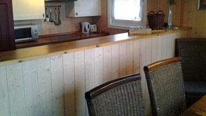 Una cocina con paneles de madera, microondas, estufa y ventana con vistas. Hay sillas de mimbre y una cesta en la encimera.