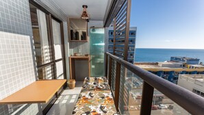 Un balcón con vista al mar, una pared de azulejos, una mesa de madera y un banco estampado.
