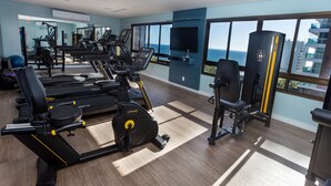 Un gimnasio con máquinas de cardio, estaciones de pesas y una televisión.