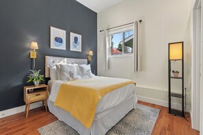 Une chambre à coucher comprenant un lit, des lampes de chevet, une table de chevet, une fenêtre avec des rideaux et un lampadaire.