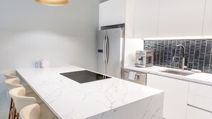 A modern kitchen with a marble island, bar stools, a refrigerator, and a coffee machine. - The Ampersand Sky Villa: Iconic, Artful Luxury (Charlotte Amalie, Saint Thomas)