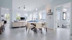 A spacious dining area with a round table and chairs, a kitchen with a large island, and large windows providing natural light. - The Ampersand Sky Villa: Iconic, Artful Luxury (Charlotte Amalie, Saint Thomas)