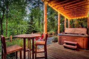 Une terrasse en bois avec un jacuzzi, une table et des chaises, le tout entouré d’une forêt.