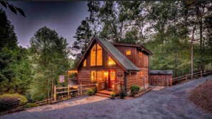 A log cabin with a porch, a garage, and a gravel driveway surrounded by trees. - Mystic Creek Retreat (next to Blue Ridge) (Mineral Bluff)