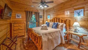 A wooden cabin bedroom with a bed, a ceiling fan, a nightstand, and wall art. - Mystic Creek Retreat (next to Blue Ridge) (Mineral Bluff)