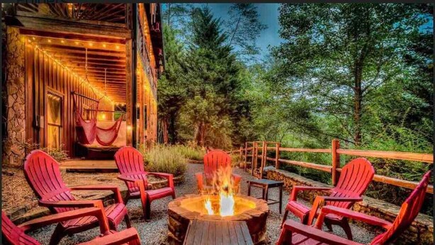 A wooden deck with red chairs and a fire pit. - Mystic Creek Retreat (next to Blue Ridge) (Mineral Bluff)