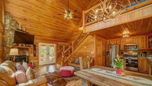 A log cabin interior with a stone fireplace, wooden staircase, and a kitchen area. - Mystic Creek Retreat (next to Blue Ridge) (Mineral Bluff)