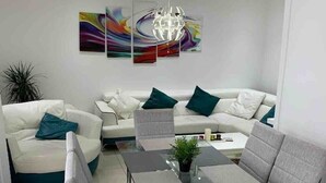 Una sala de estar moderna con una mesa de comedor de vidrio, sillas tapizadas en gris, un sofá blanco con cojines color turquesa y arte abstracto en la pared.