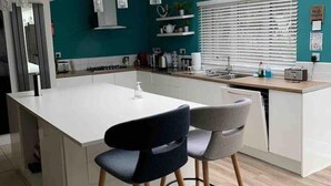 Una cocina moderna con una isla central, dos taburetes de bar y una ventana con persianas.