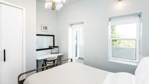 Une chambre à coucher avec un lit, un bureau et une chaise, un miroir, une fenêtre et une porte.