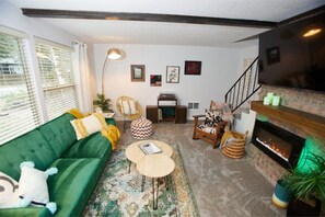 Un salon chaleureux avec un canapé vert, une table basse, une cheminée et un escalier.