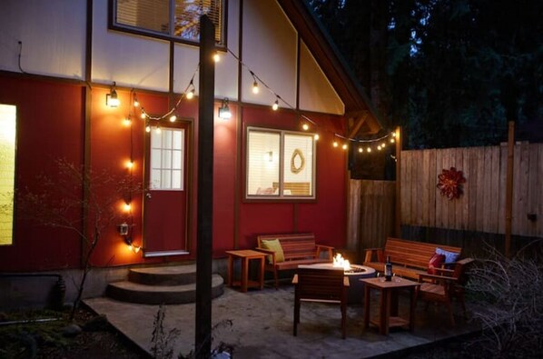 Un espace extérieur accueillant, aménagé avec un foyer, des guirlandes lumineuses et une clôture en bois.