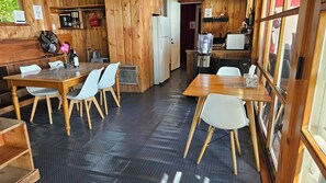 Ein Holzinnenraum mit Tischen, Stühlen, einem Kühlschrank und einem Wasserspender.