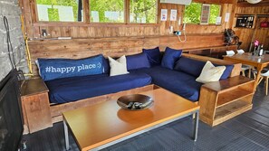 Un interior de madera con un sofá, una mesa y vistas al exterior con vegetación.