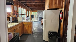 A rustic kitchen with wooden cabinets, a stone wall, a refrigerator, and a microwave.
