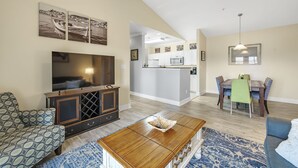 A modern living room with a TV, sofa, coffee table, and dining area with a table and chairs. - Spacious Condo minutes from the Beach and Foley Outlets (Foley)