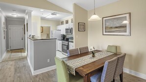 A modern kitchen with white cabinets, a central island, and a dining area with a wooden table and patterned runner. - Spacious Condo minutes from the Beach and Foley Outlets (Foley)