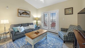 A living room with a gray sofa, a wooden coffee table, a patterned armchair, and a ceiling fan. - Spacious Condo minutes from the Beach and Foley Outlets (Foley)