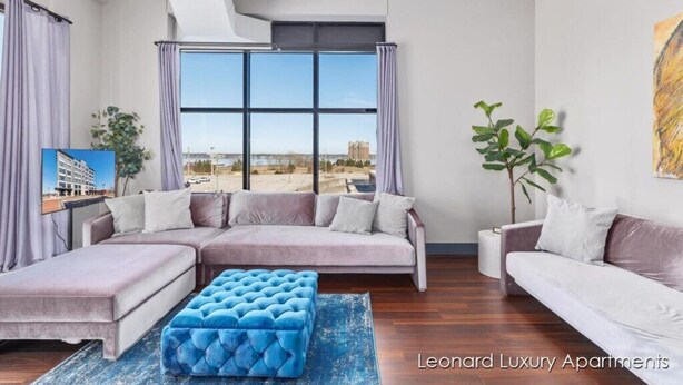 A modern living room with a sectional sofa, a blue ottoman, and a large window offering a city view.
