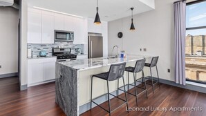A modern kitchen with white cabinets, a marble island, and black pendant lights.