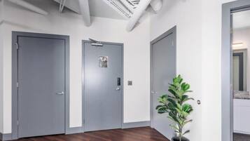 Un couloir avec trois portes grises, une plante en pot et des conduits apparents au plafond.