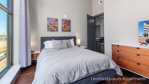 A modern bedroom with a large bed, a dresser, and two artworks on the wall.