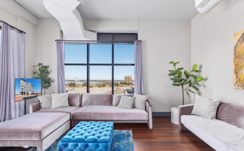 A modern living room with a sectional sofa, a blue ottoman, and a large window offering a city view.