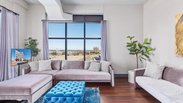 A modern living room with a sectional sofa, a blue ottoman, and a large window offering a city view.