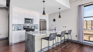 A modern kitchen with white cabinets, a marble island, and black pendant lights.
