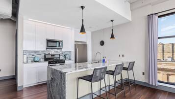 A modern kitchen with white cabinets, a marble island, and black pendant lights.