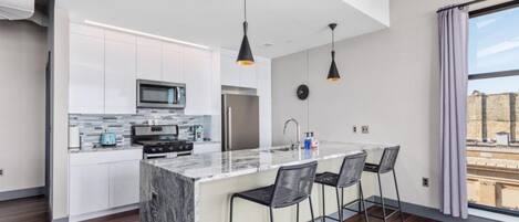 A modern kitchen with white cabinets, a marble island, and black pendant lights.