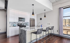 A modern kitchen with white cabinets, a marble island, and black pendant lights.