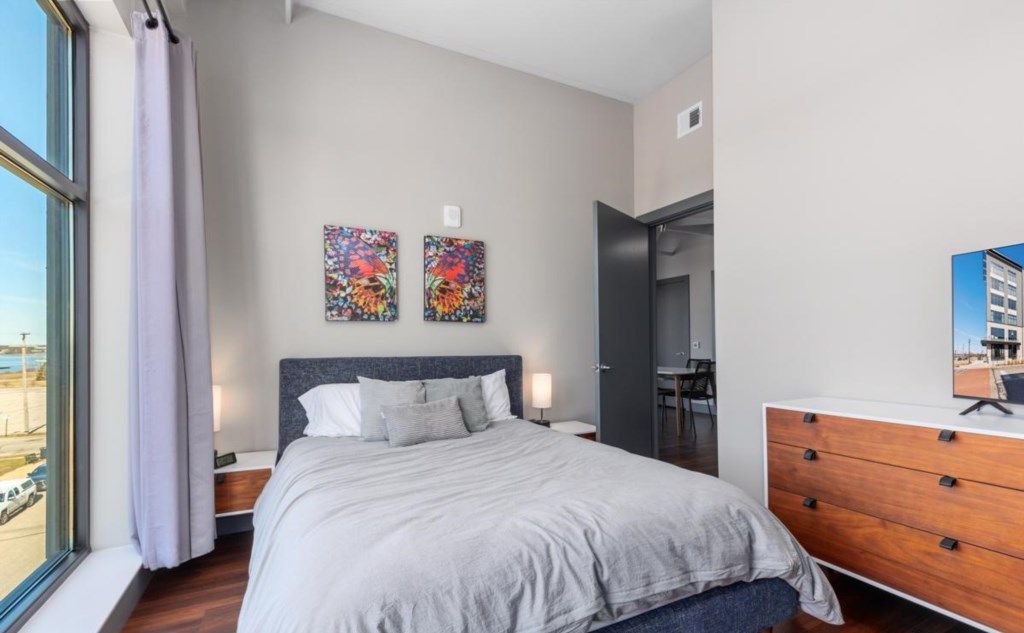 Une chambre à coucher moderne avec un grand lit, une commode et deux œuvres d’art accrochées au mur.