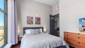 A modern bedroom with a large bed, a dresser, and two artworks on the wall.
