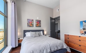 A modern bedroom with a large bed, a dresser, and two artworks on the wall.