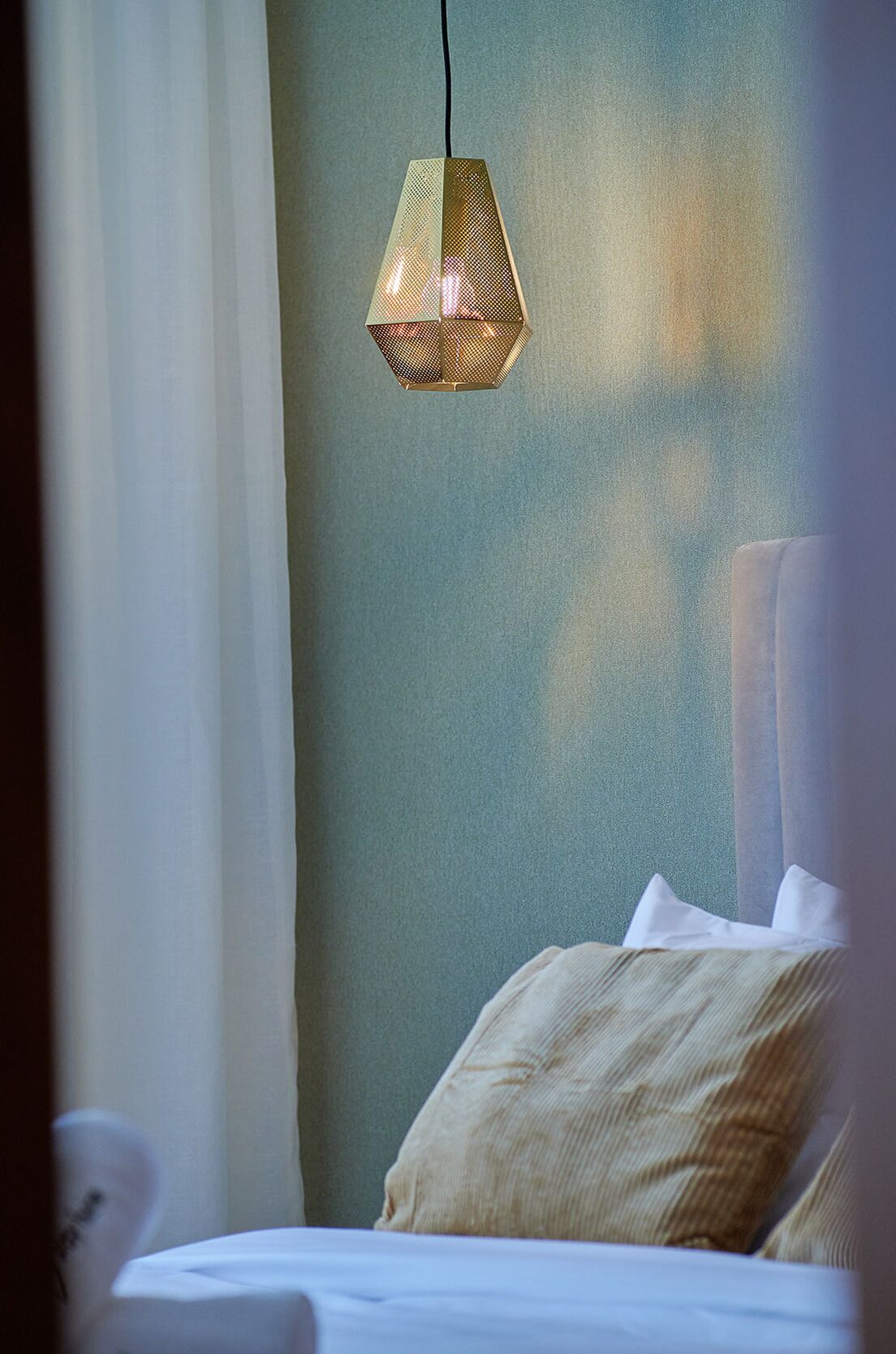 A bedroom with a bed, a hanging light fixture, and a green wall.
